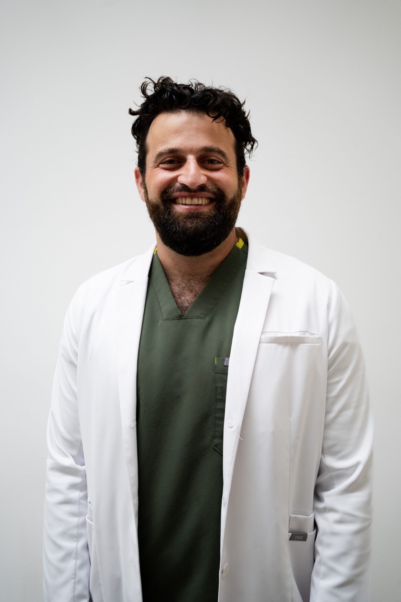Benjamin Leventer smiling in a white coat and green scrubs